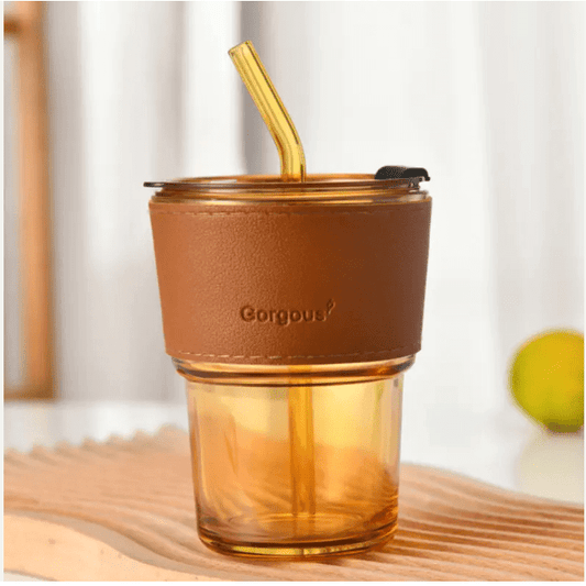 Stylish amber glass cup with a brown leather sleeve and straw, perfect for enjoying drinks on the go.